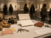Objetos cotidianos expuestos en una vitrina de museo contemporáneo mientras varios visitantes observan la colección