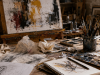 Mesa de trabajo de un artista con bocetos arrugados, manchas de pintura y materiales creativos que evocan el papel del azar en el proceso artístico