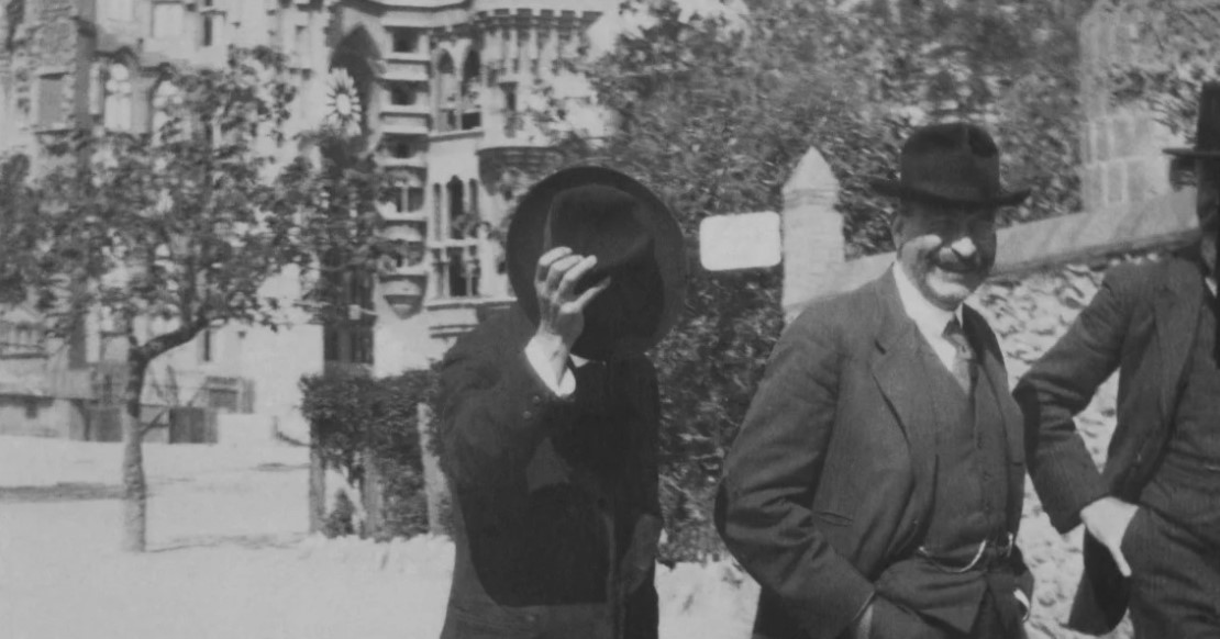 Antoni Gaudi tapándose la cara con un sombrero delante la Sagrada Familia.1920
