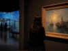 Visitante contempla una obra real en una sala de museo con una proyección inmersiva al fondo