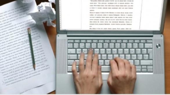 persona escribiendo en laptop y con manuscrito cerca 